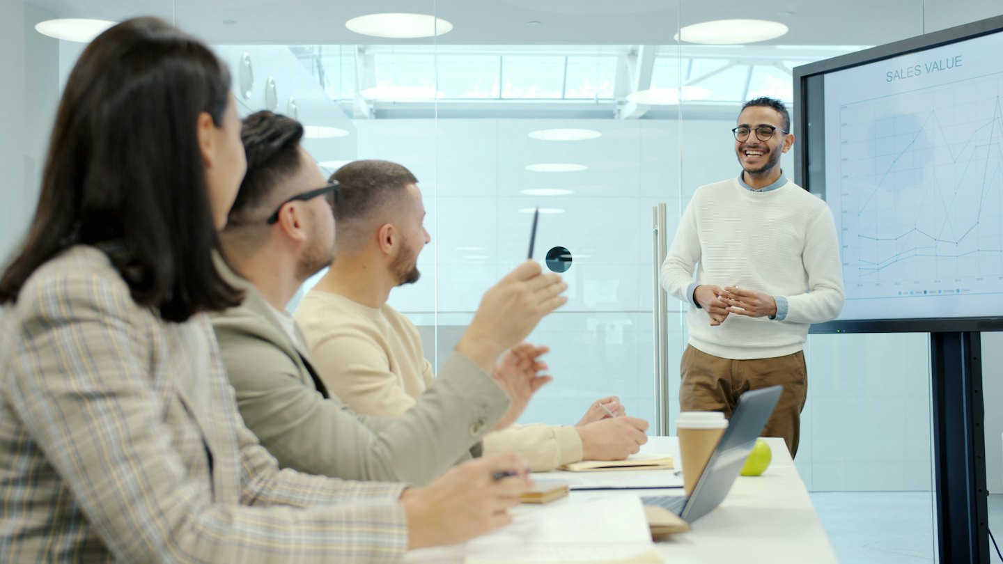 Man presents sales graph to colleagues in office conference room.